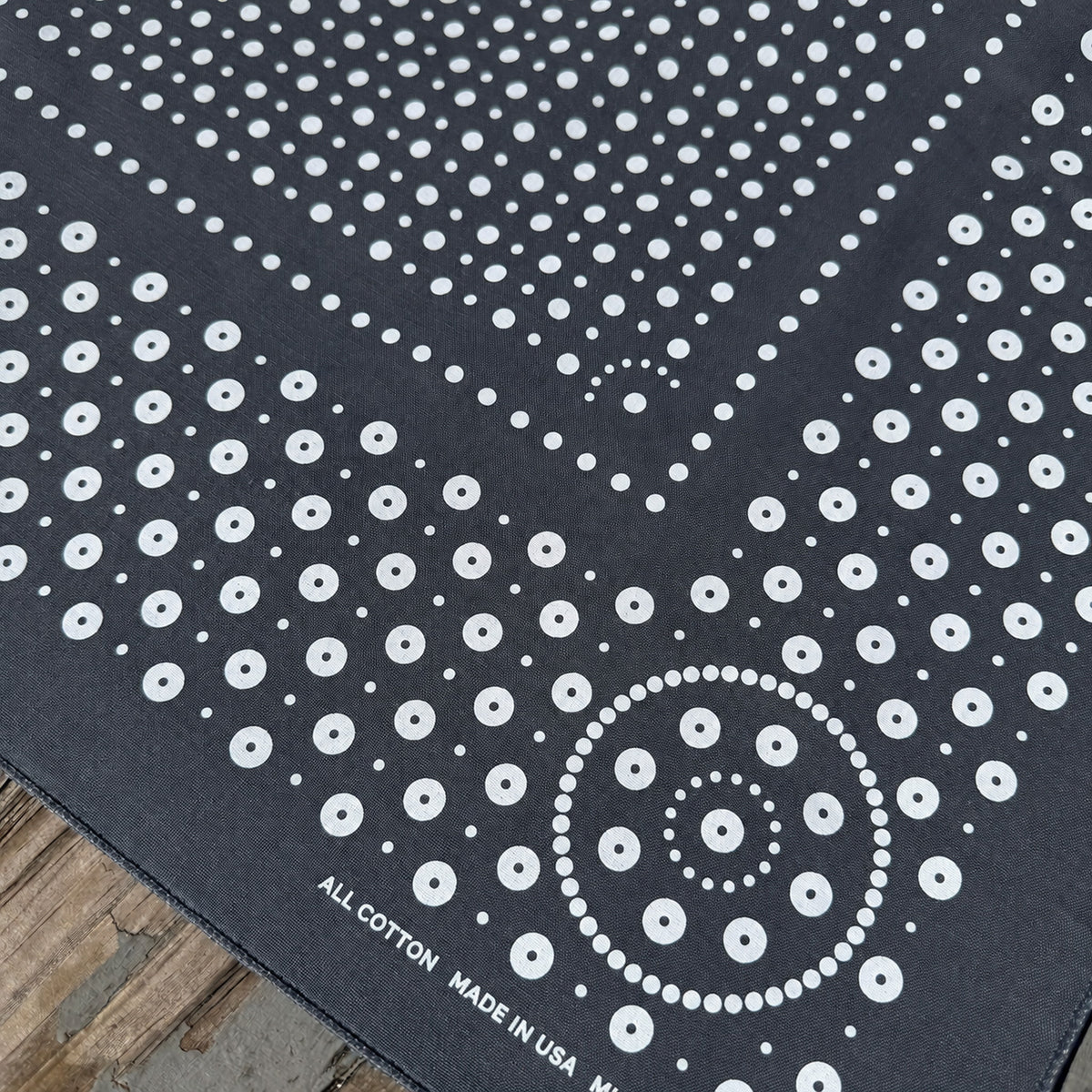 Rivet bandana in Gray with white dot print, corner detail showing the concentric dot medallion, on weathered wood