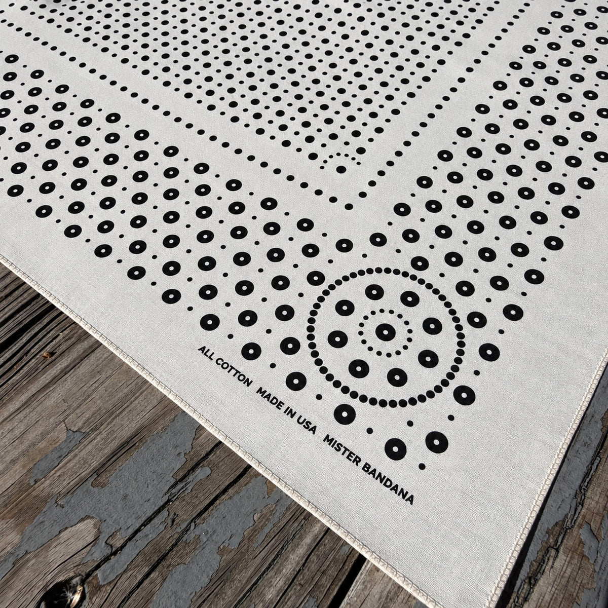Rivet bandana in Rattan (natural off-white) with black dot print, corner detail with stitched hem, on weathered wood